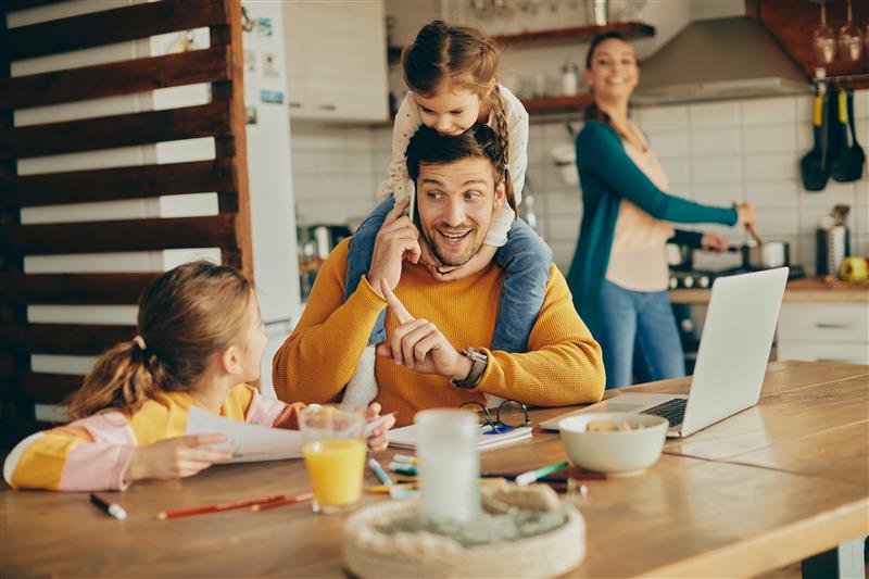 Family of four in a kitchen. A man with two little girls on the tablea nd woman on the stove on the back.